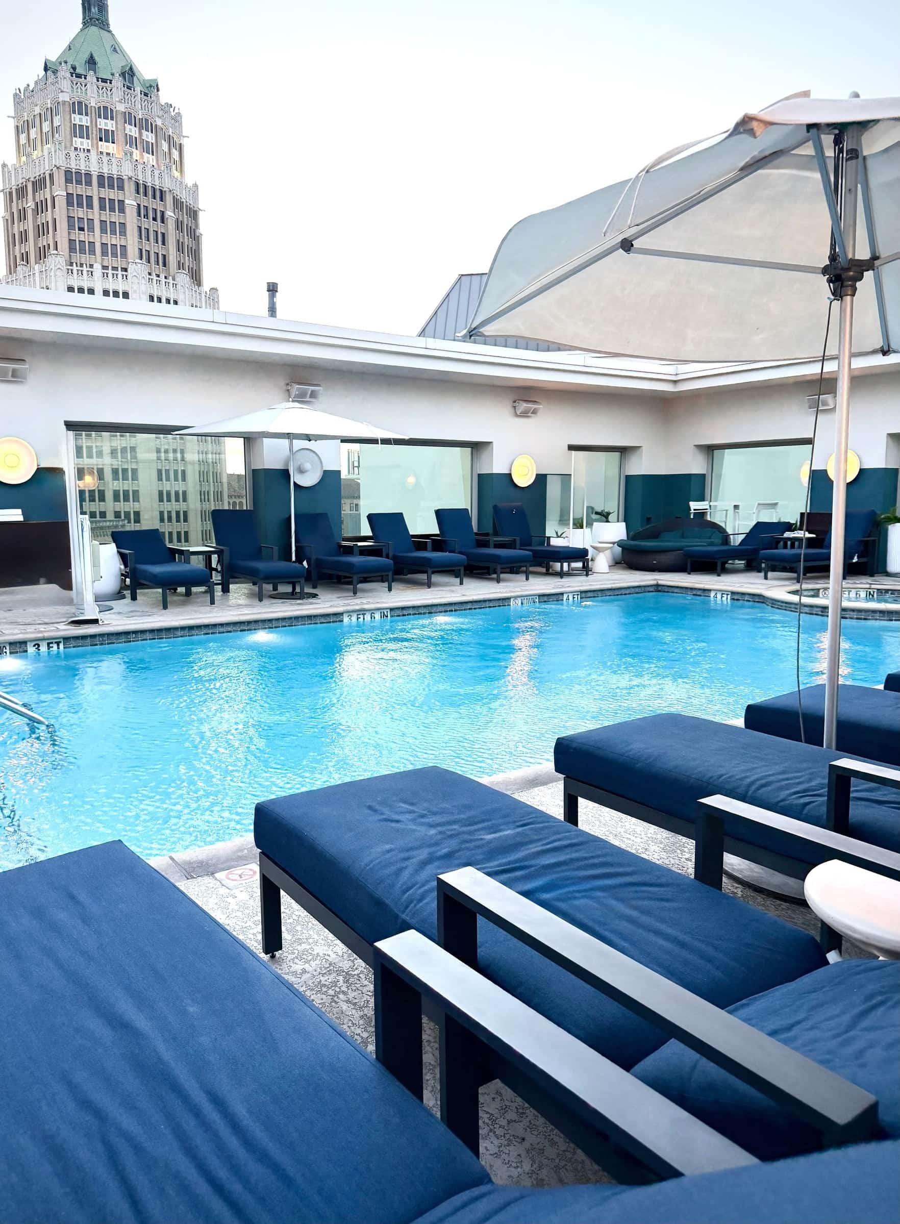 Rooftop pool lined with navy loungers and umbrellas beneath a historic downtown tower