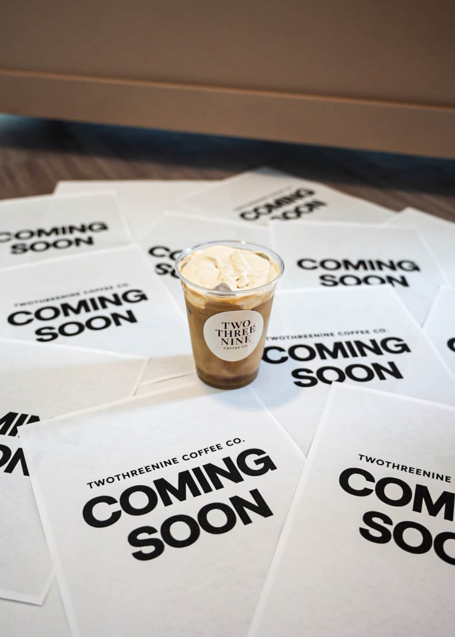 Iced latte resting on a spread of Coming Soon flyers for a new café opening