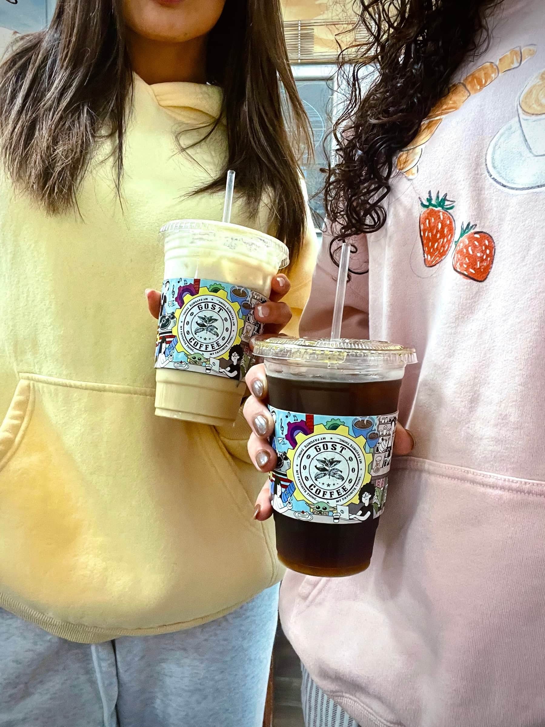 Two people in a yellow hoodie and a strawberry sweater holding iced drinks in illustrated cups