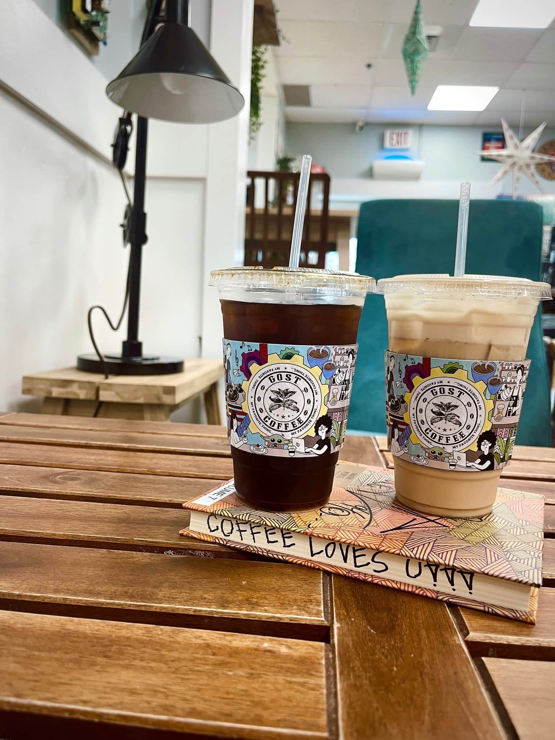Two iced coffees in illustrated cups resting on a Coffee Loves You book on a sunlit wooden table