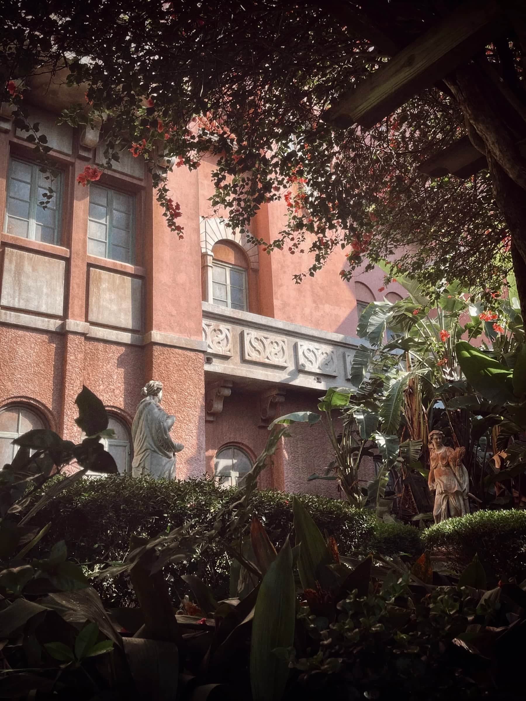 Pink stucco courtyard with bougainvillea, palms and classical statues in dappled light