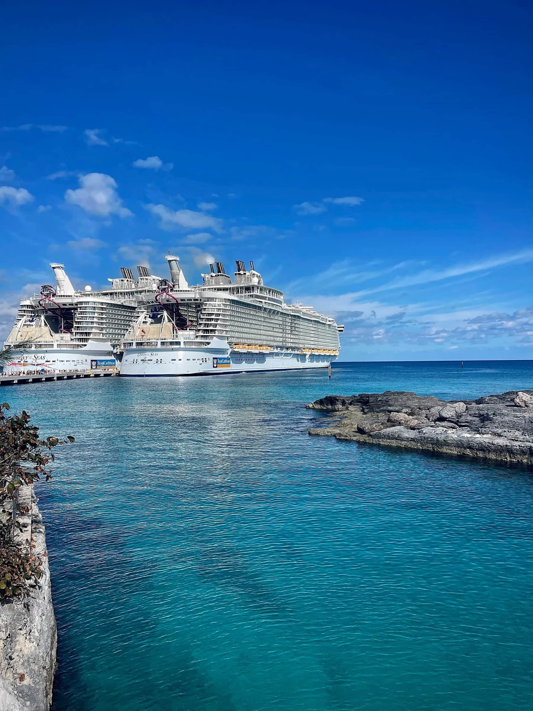Cruise ship docked beside a turquoise cove and rocky shoreline under a bright blue sky