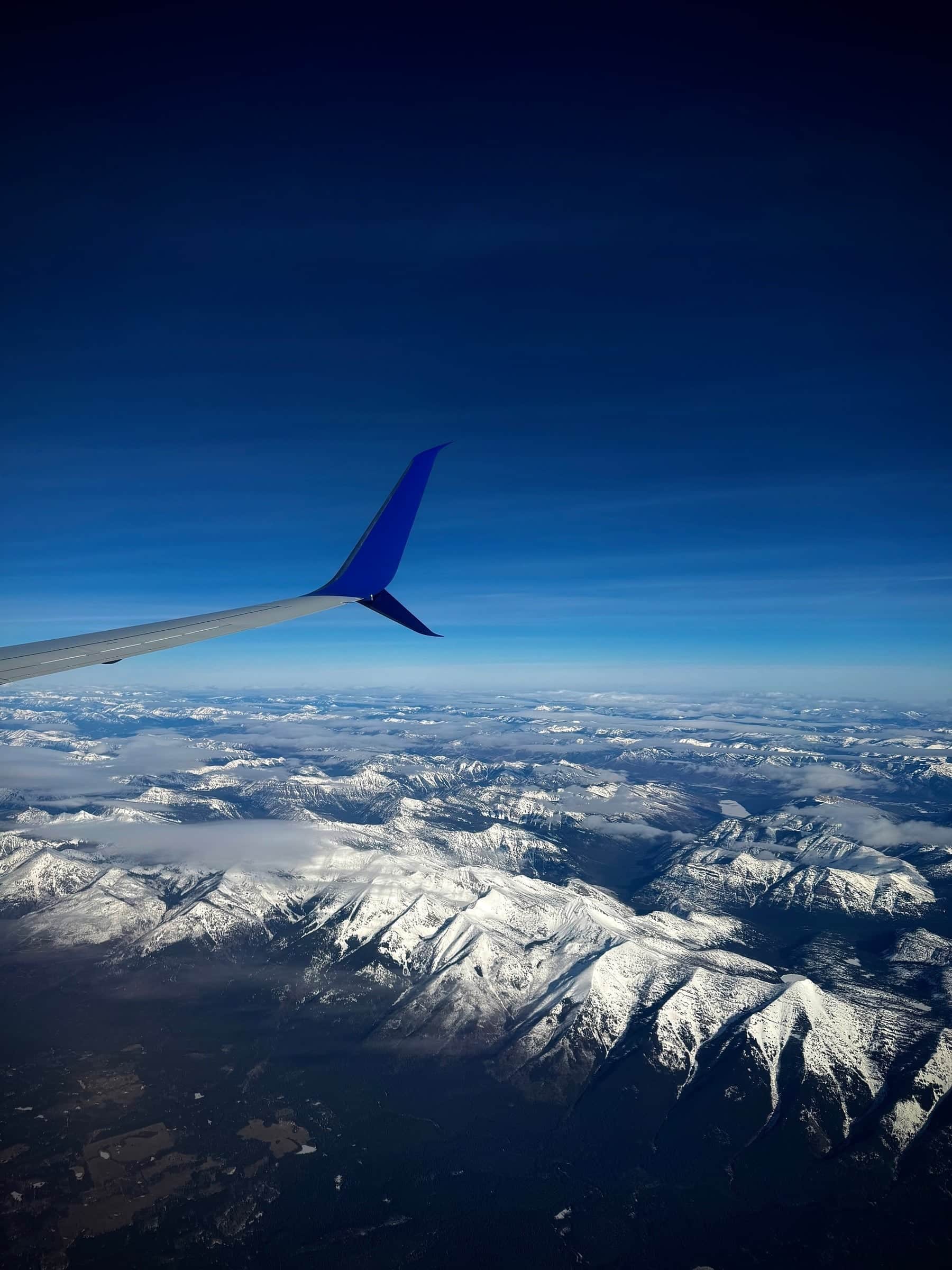 Snow covered mountain ranges seen from a plane window beneath an airplane wing