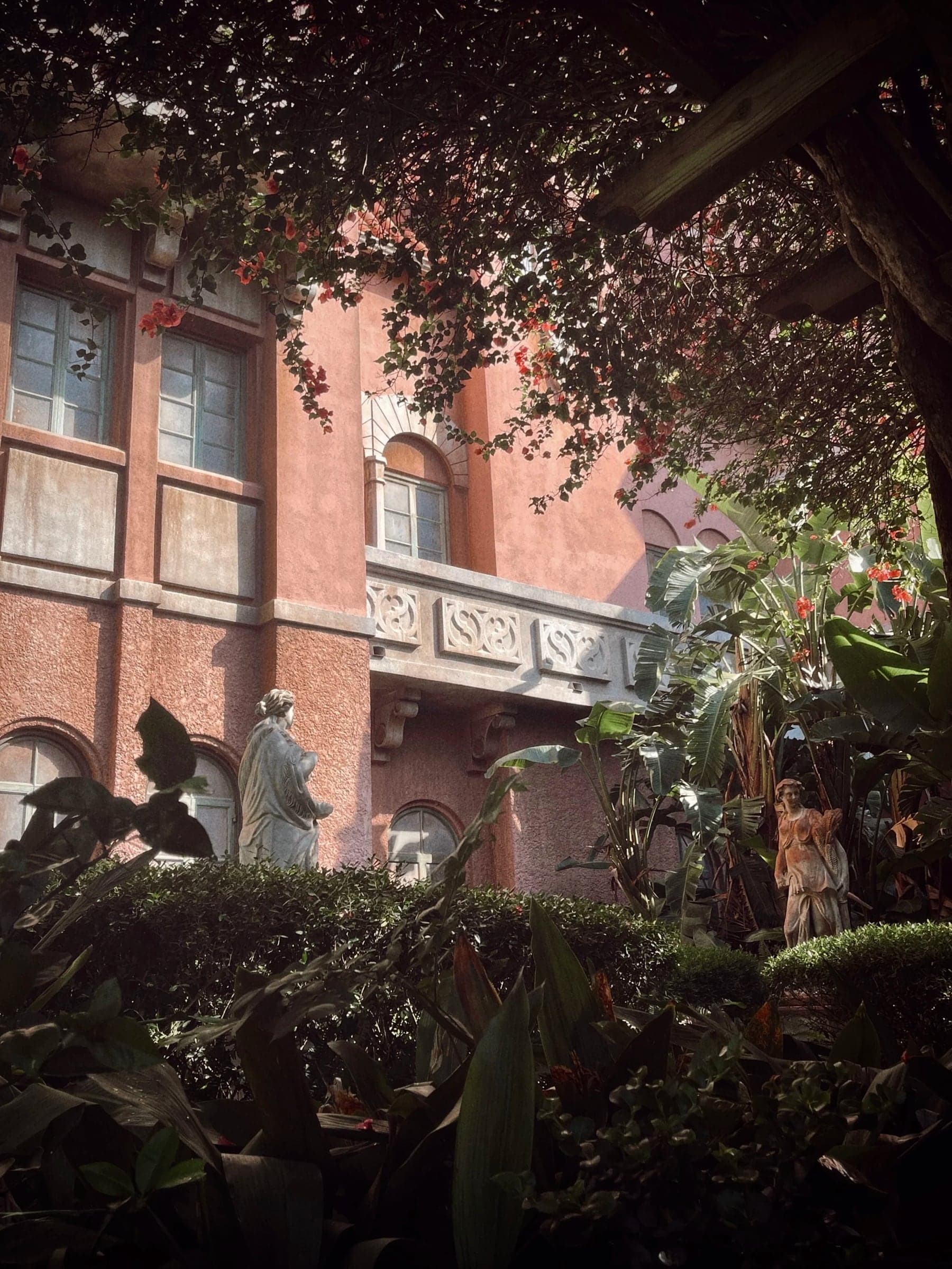 Pink stucco courtyard with bougainvillea, palms and classical statues in dappled light