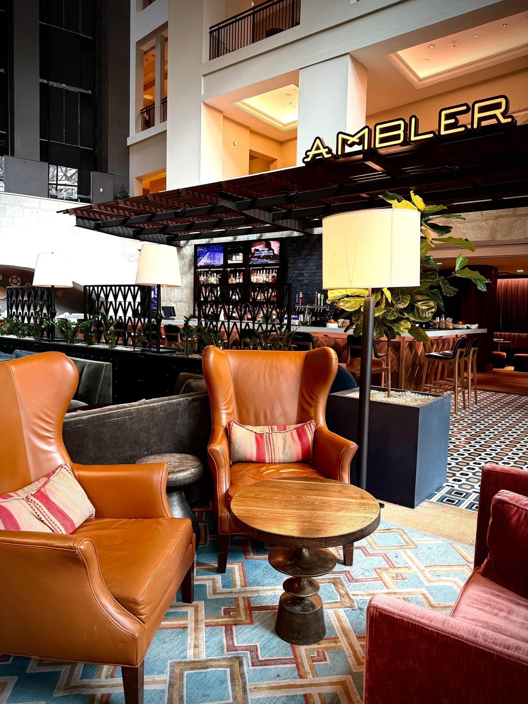 Cognac leather armchairs on patterned tile in the Ambler lounge beneath its illuminated sign