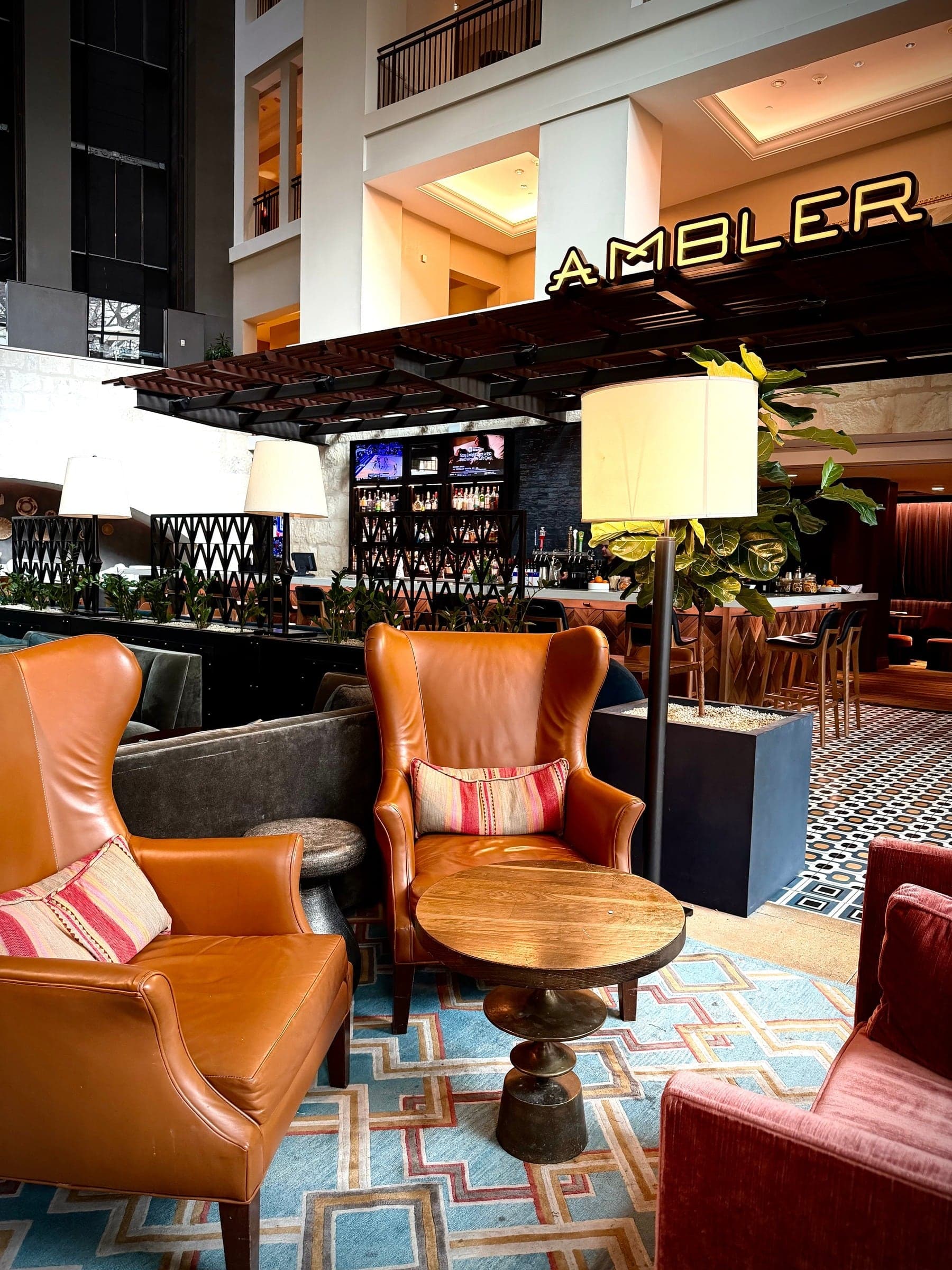 Cognac leather armchairs on patterned tile in the Ambler lounge beneath its illuminated sign