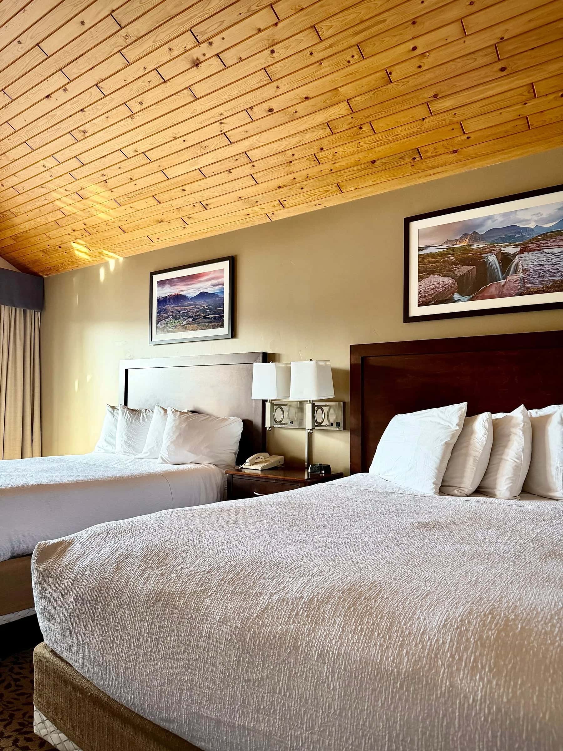 Guest room with a warm pine ceiling, crisp white bedding and framed mountain prints