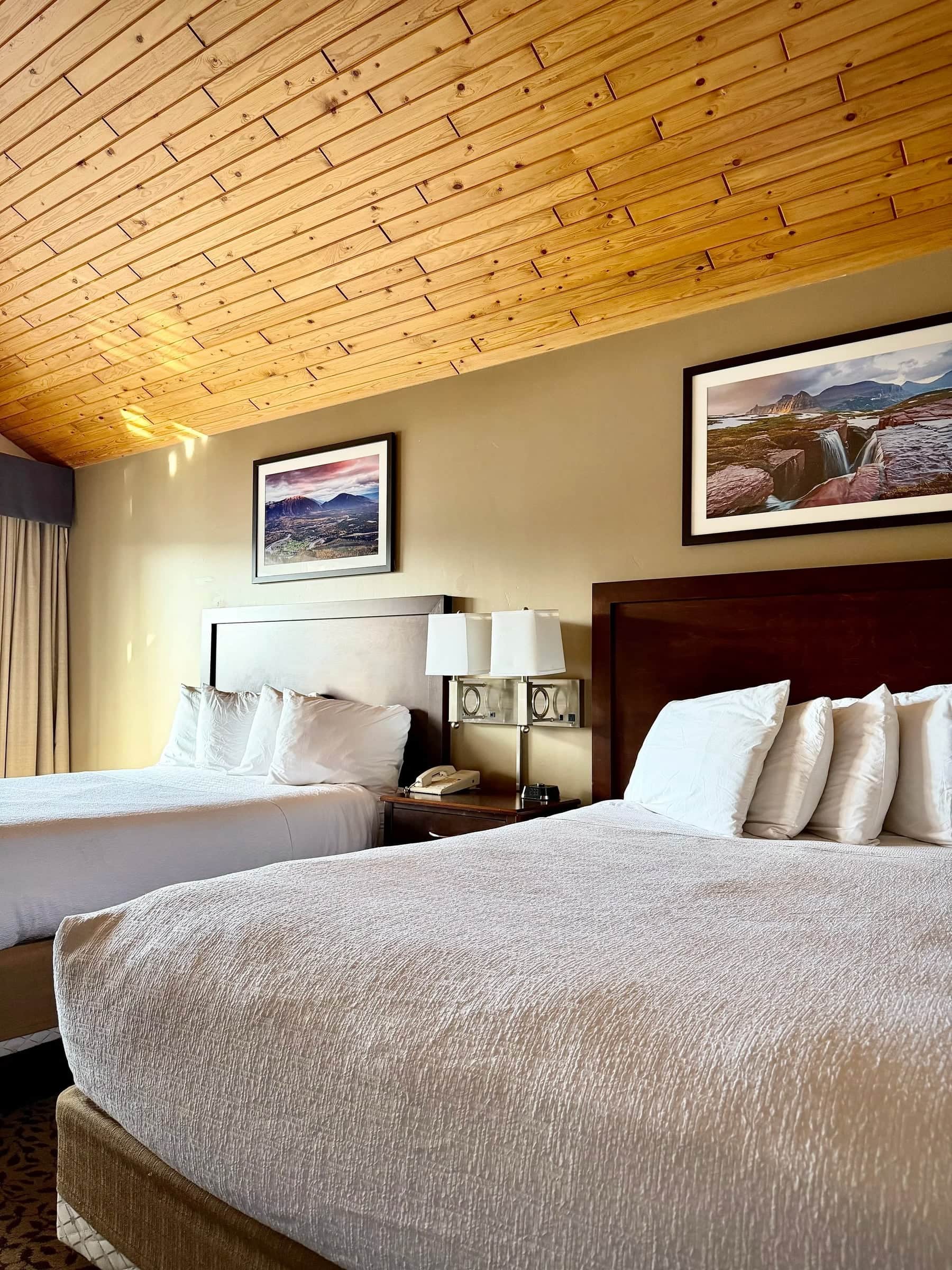 Guest room with a warm pine ceiling, crisp white bedding and framed mountain prints