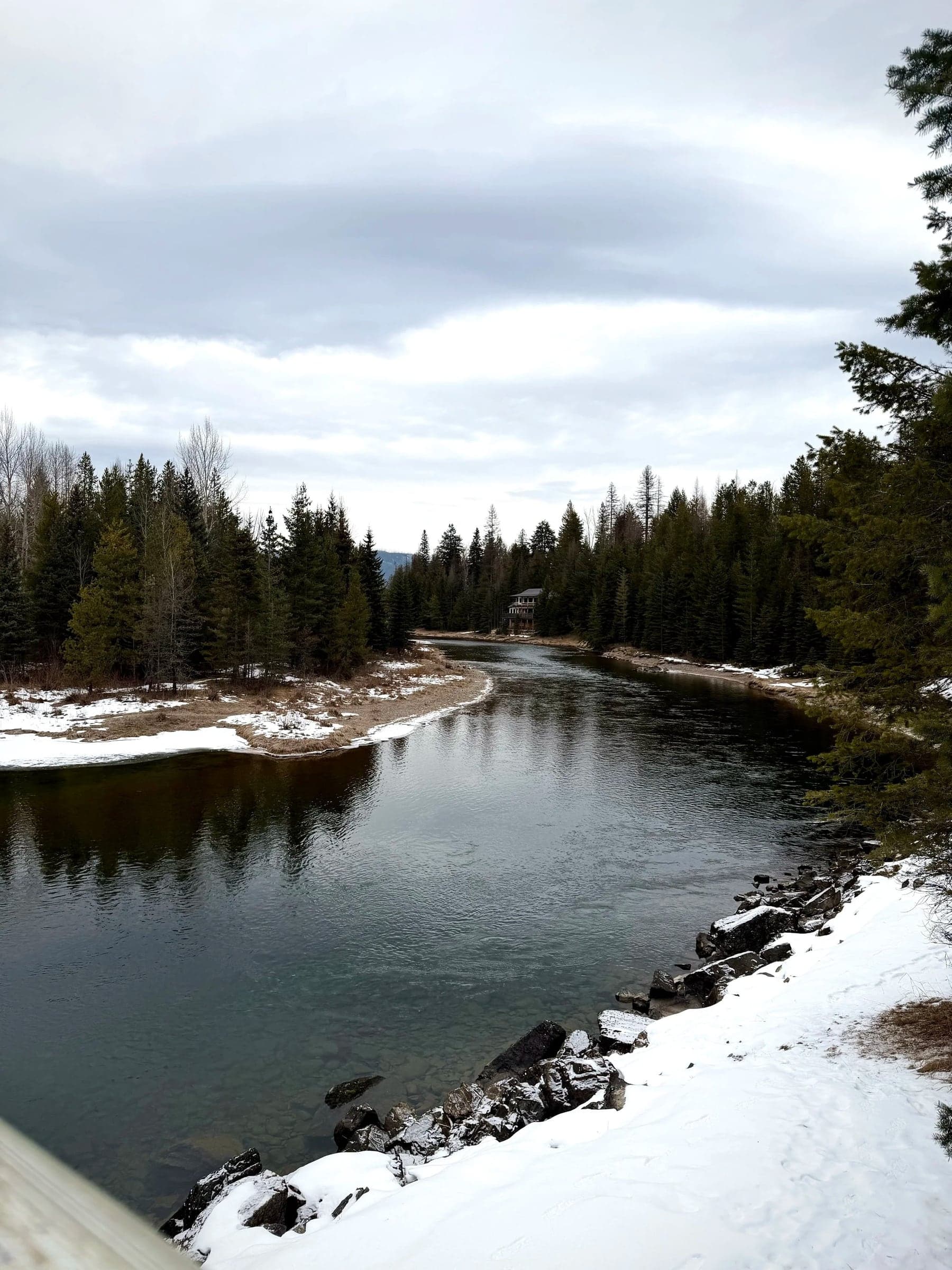 The Whitefish River winding between snowy banks and pine trees under a soft winter sky